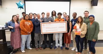 Brad Love standing in center of image holding check, surrounded by students 
