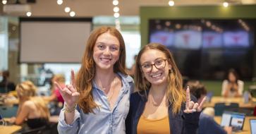 Two students smile and hold up a "hook 'em" hand sign. 