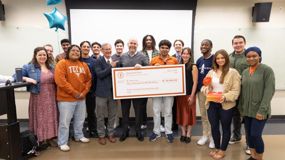 Brad Love standing in center of image holding check, surrounded by students 