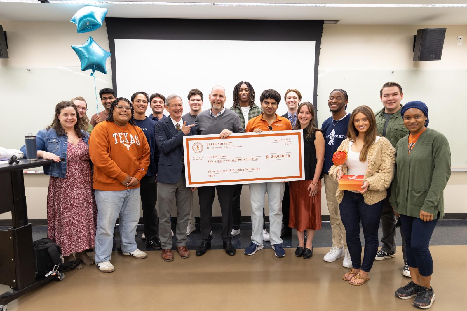 Brad Love standing in center of image holding check, surrounded by students 