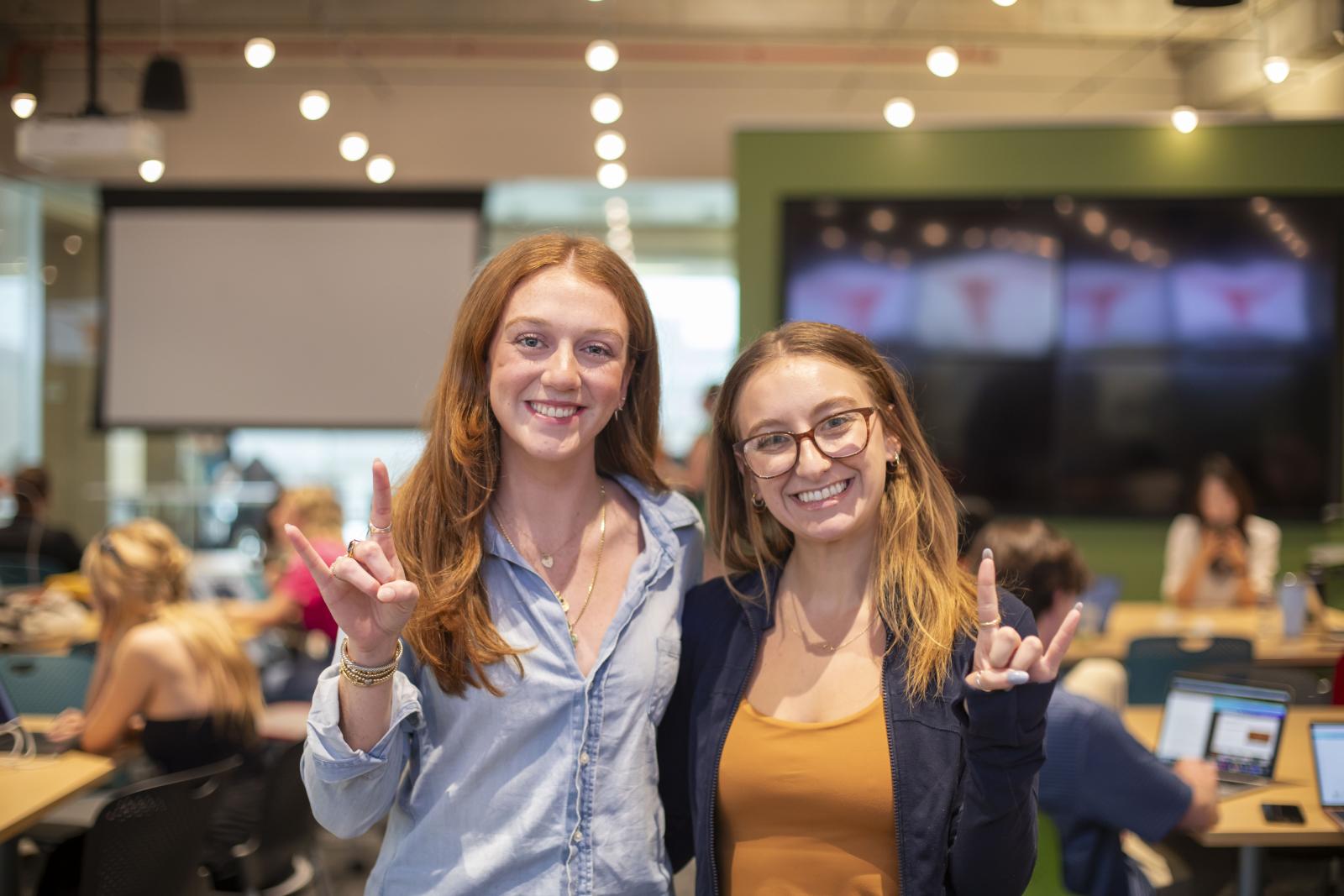 Two students smile and hold up a "hook 'em" hand sign. 
