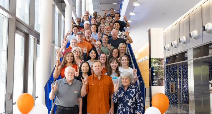 photo of SRS faculty and staff standing on steps, doing hook 'em hand sign